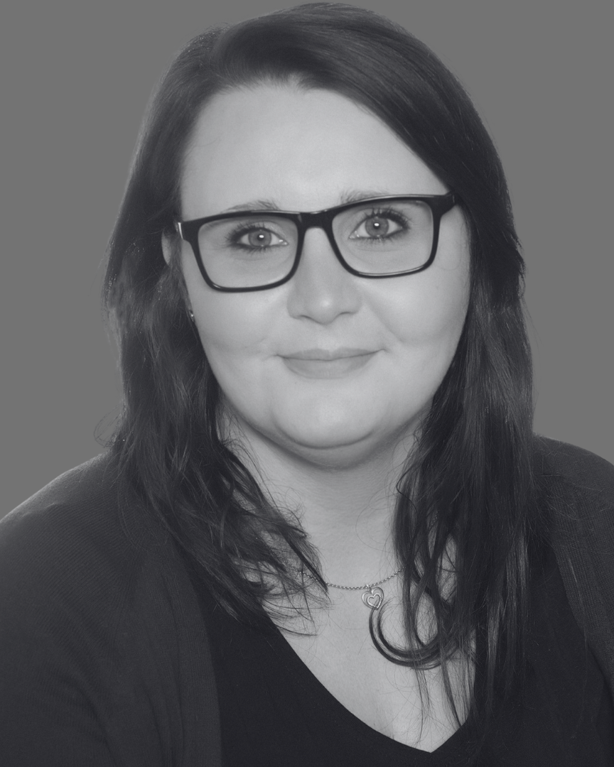 Porträt einer Frau mit langen, dunklen Haaren und einer Kette, die eine Brille trägt.