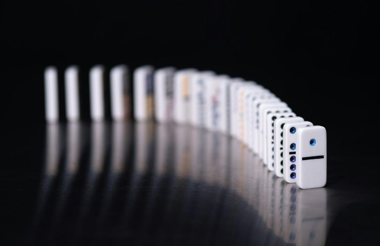 Weißes Dominospiel mit einer Reihe aufgestellter Steine in unterschiedlichen Anordnungen.