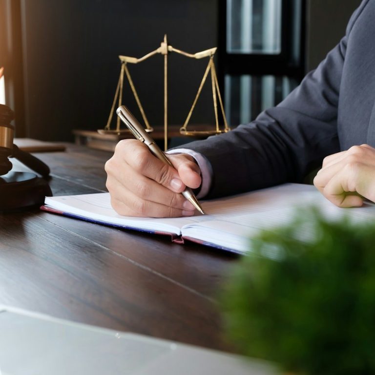 Eine Hand schreibt in ein Notizbuch, im Hintergrund eine Waage und ein Pflanze.