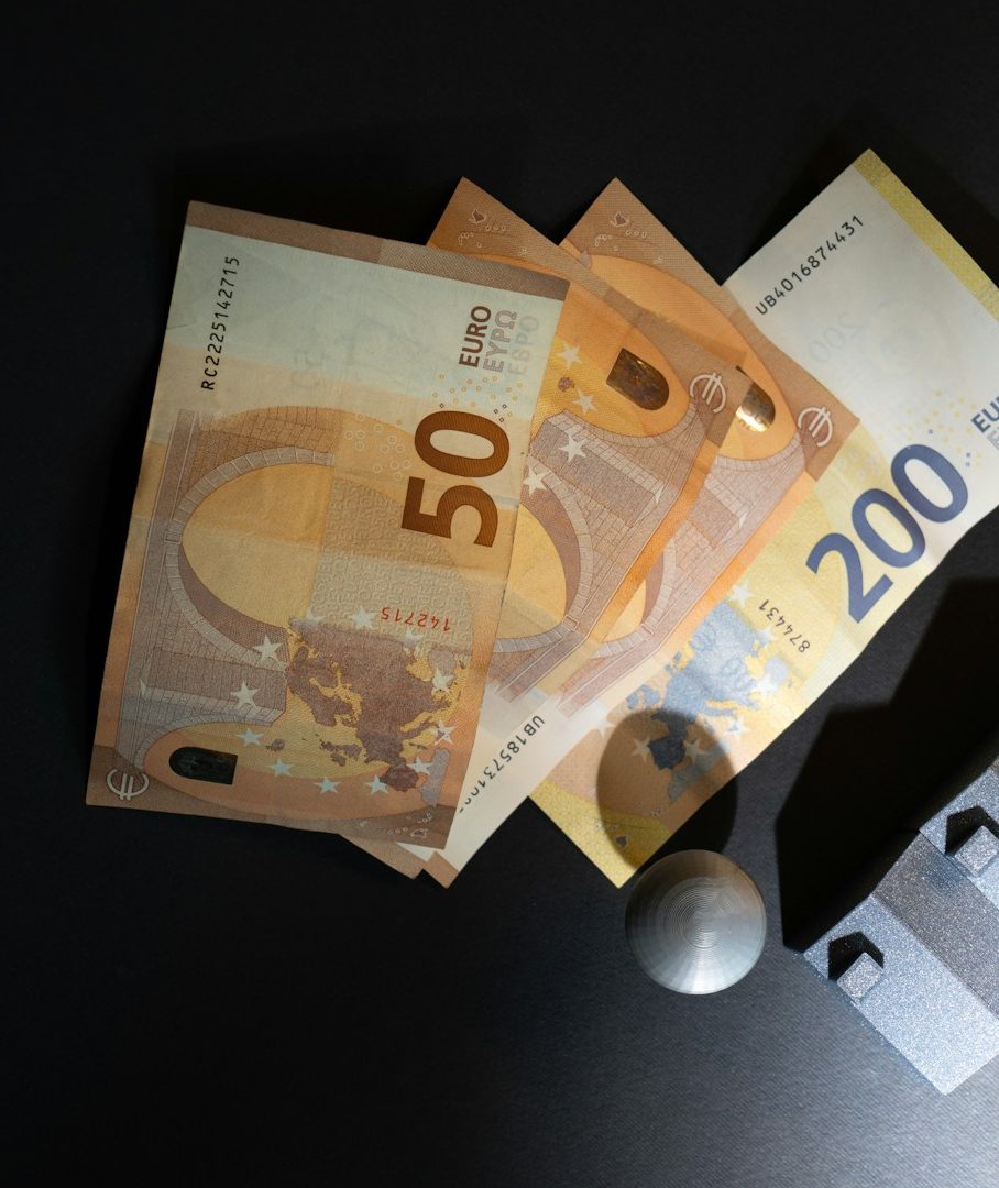 Zwei 50-Euro-Scheine, ein 200-Euro-Schein und eine Münze auf einem dunklen Hintergrund.