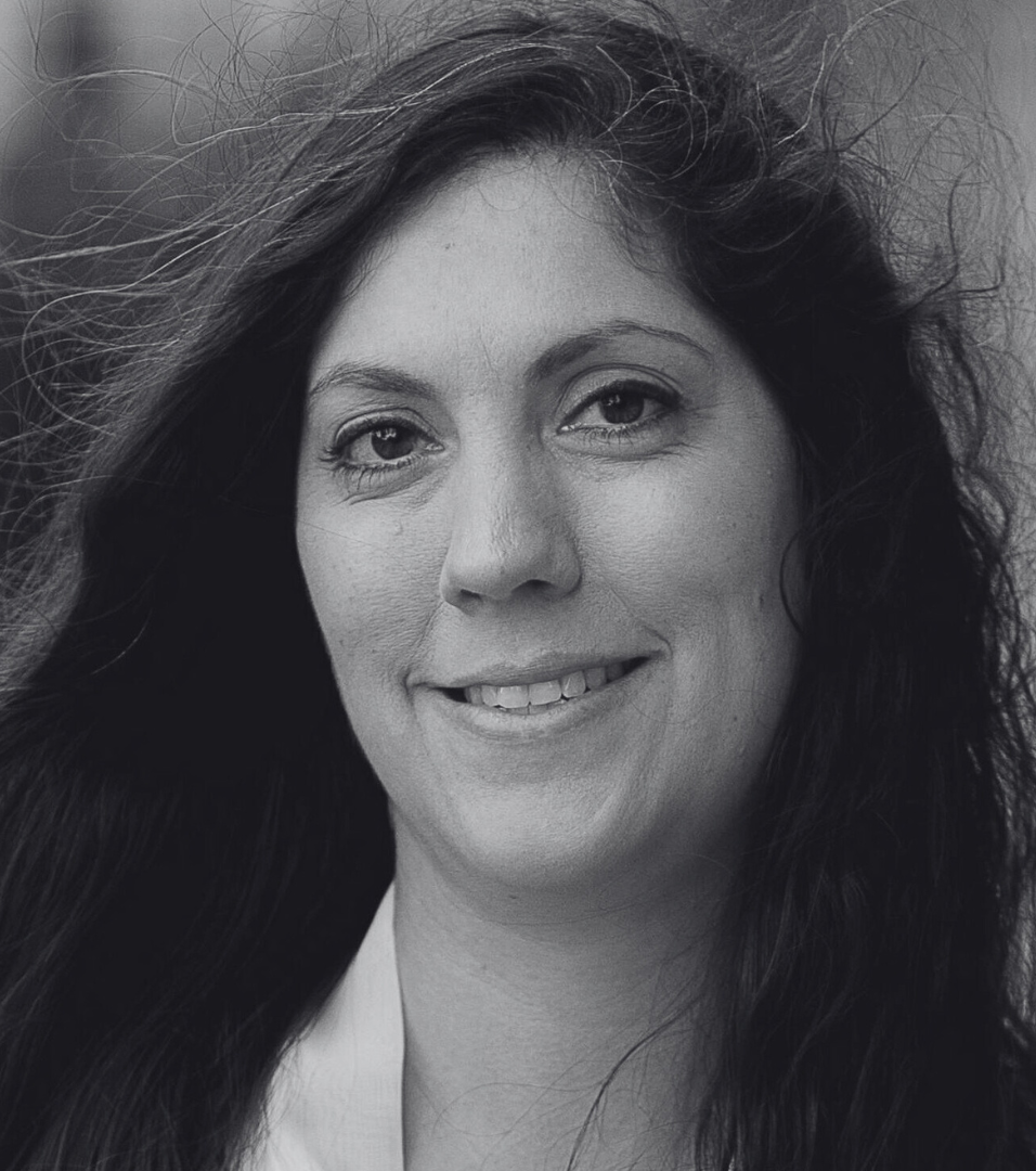 Porträt einer Frau mit langen, lockigen Haaren und freundlichem Lächeln.