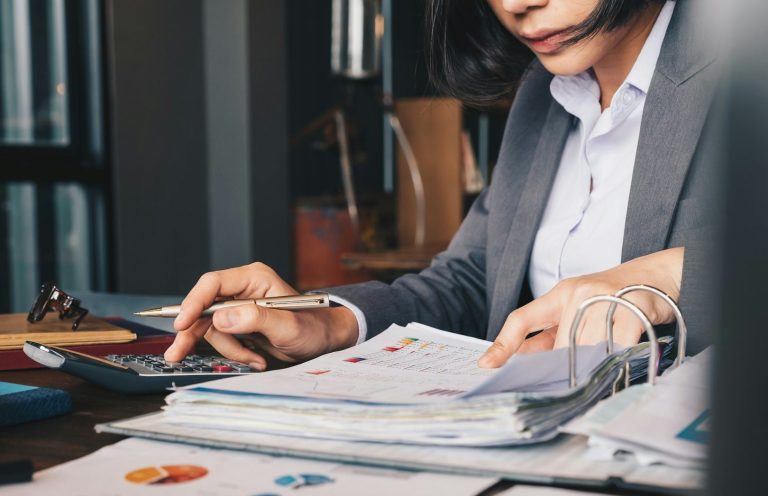 Eine Frau in einem Anzug arbeitet mit einem Taschenrechner und Finanzunterlagen.